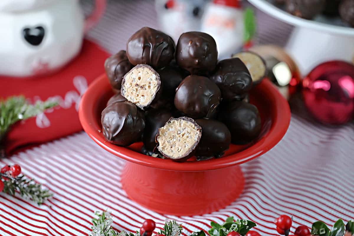 A small plate of chocolate covered peanut butter balls with Rice Krispie cereal inside. One is cut open to see the inside.