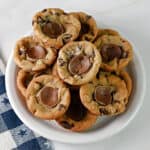 A small white plate stacked with Rolo stuffed chocolate chip cookie cups.