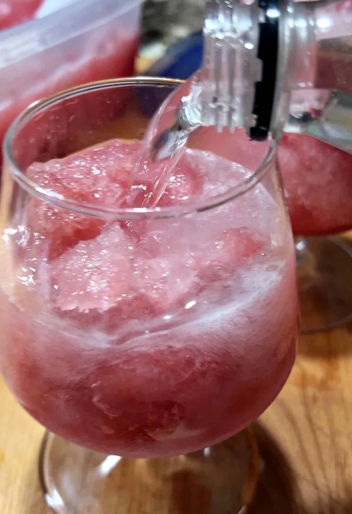 Adding lemon-lime soda to the glass to top the drink.