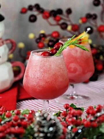 2 glasses of cranberry daiquiri rum slush garnished with cranberries, rosemary, and orange.