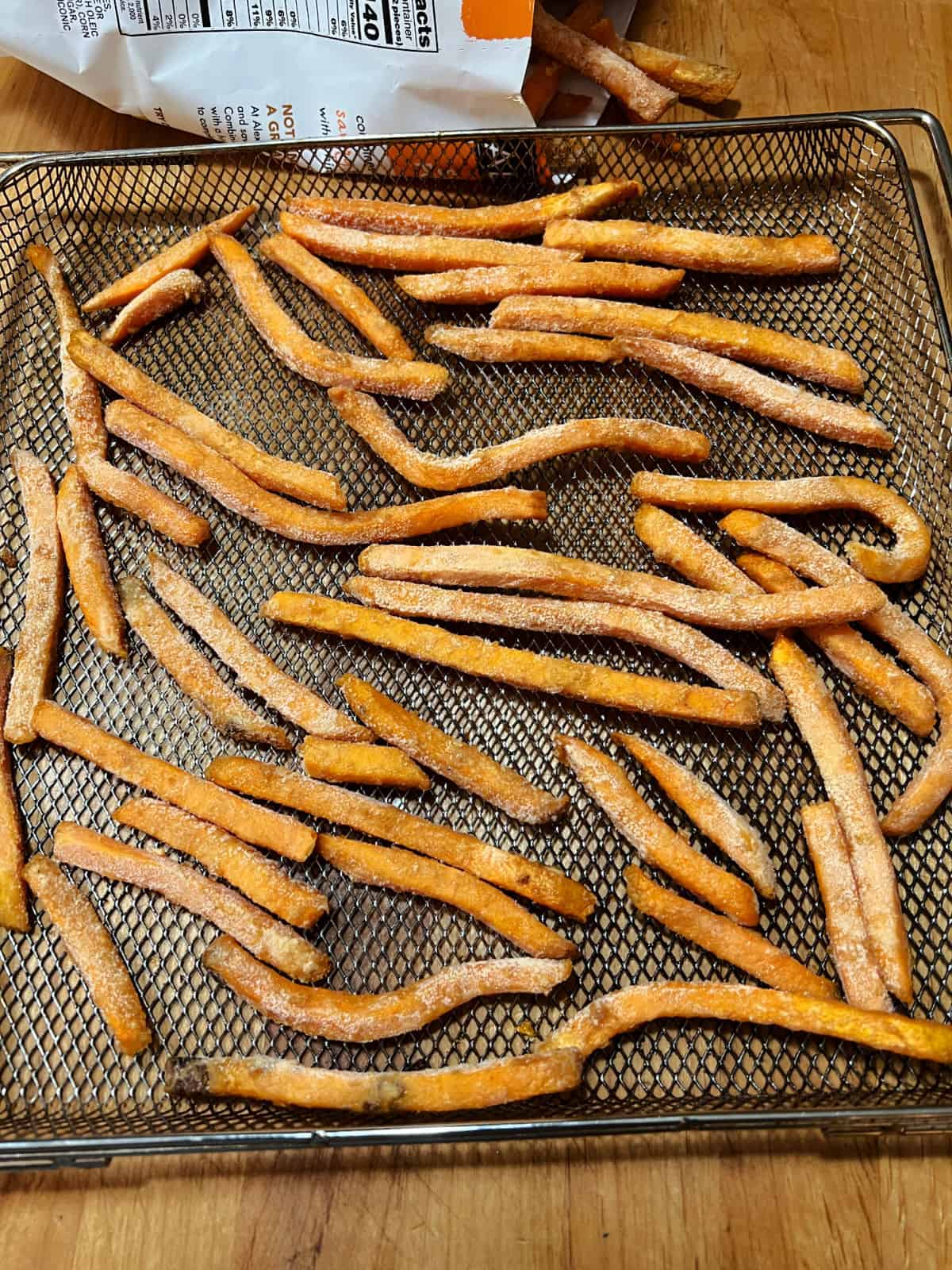 A single layer of frozen sweet potato fries in an air fryer basket.