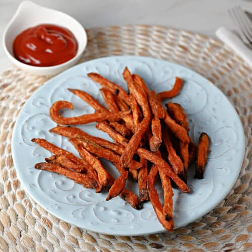 Plate of cooked sweet potato fries with some ketchup nearby for dipping.