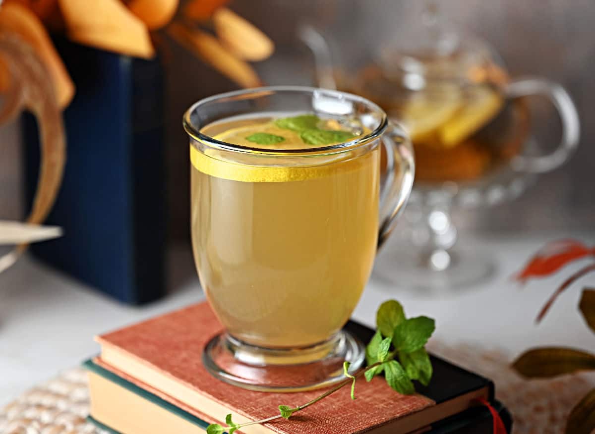 Clear mug of medicine ball tea garnished with lemon and mint.