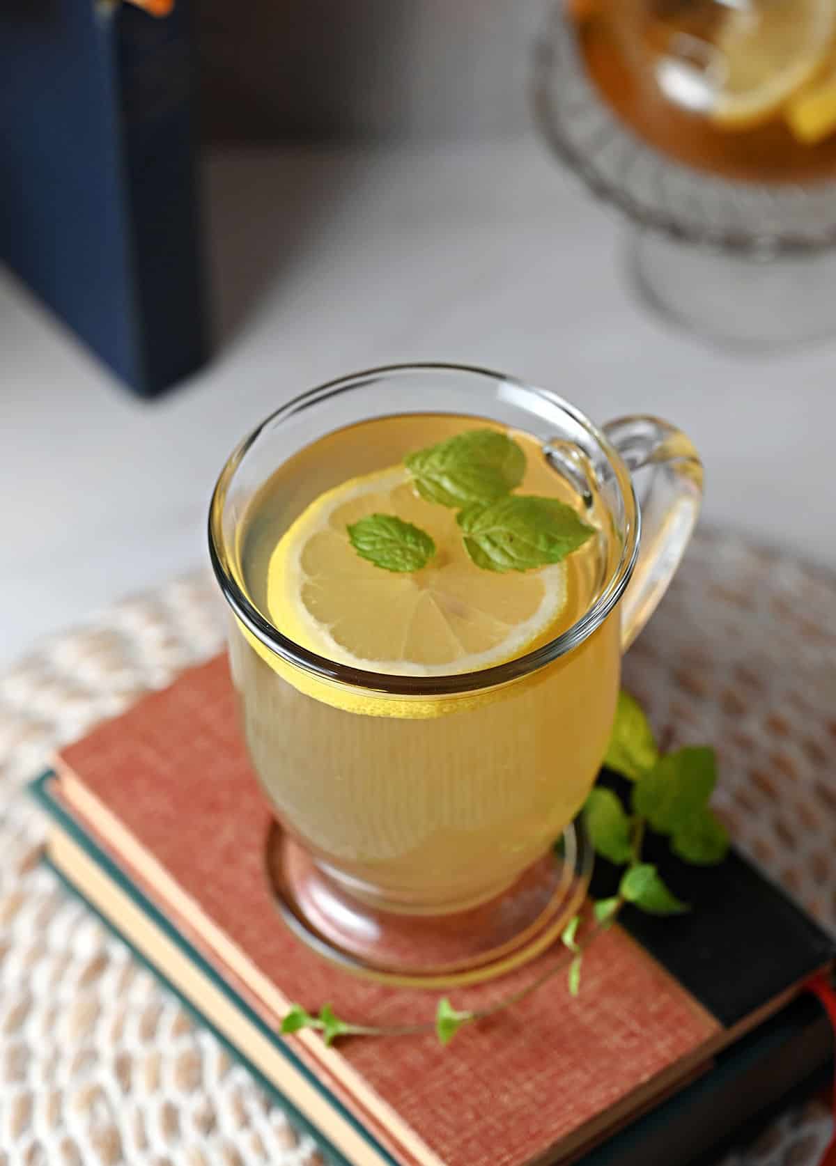 Top down view of a cup of Medicine Ball/Medicine Bomb tea garnished with a slice of lemon and 3 mint leaves.