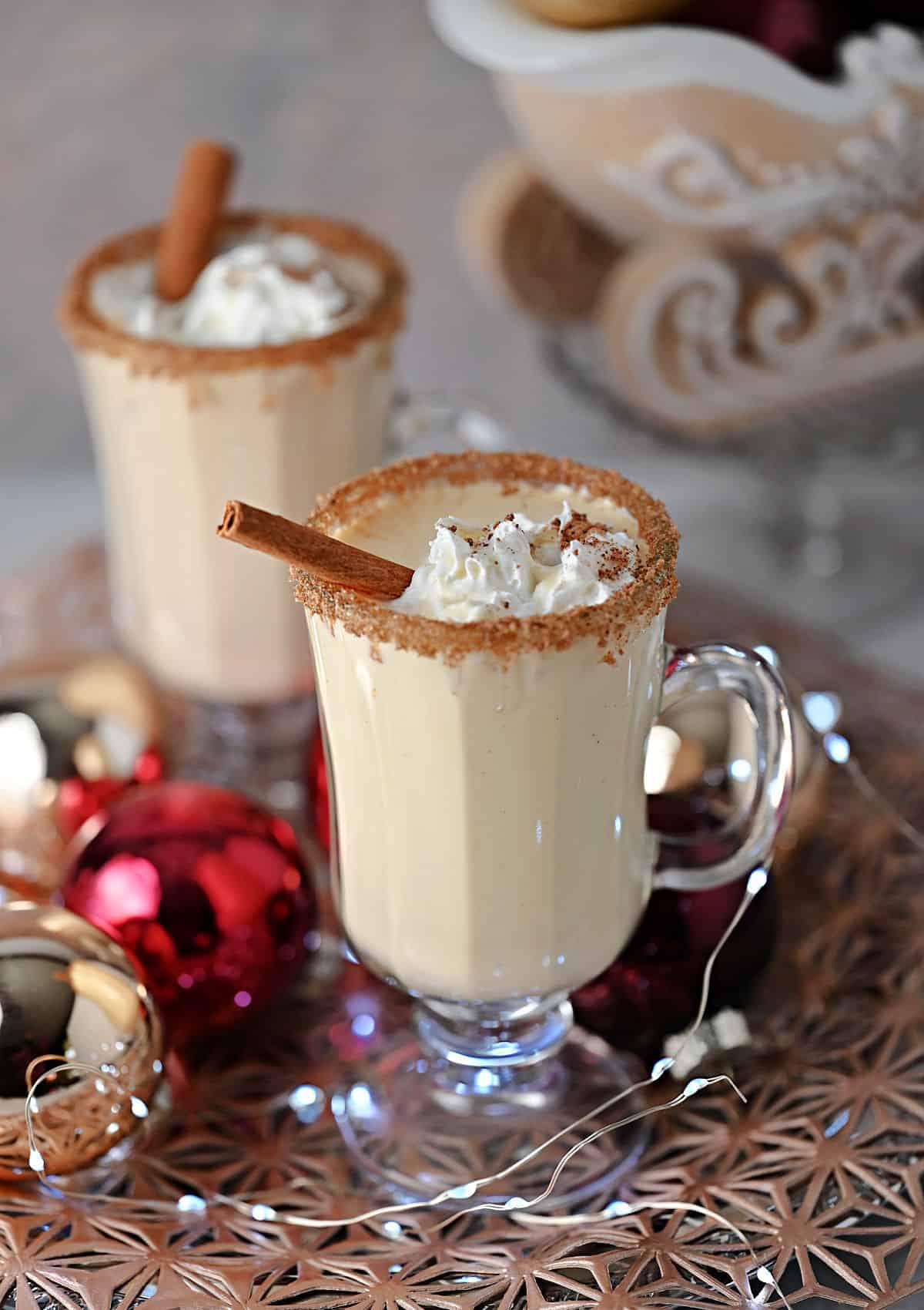 Eggnog Baileys cocktail garnished with whipped cream and nutmeg, plus a cinnamon stick.
