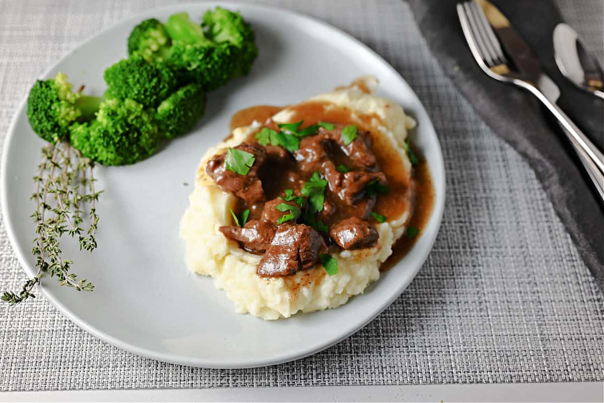 Beef tips and gravy on potatoes served with broccoli.