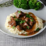 Instant Pot Beef Tips and gravy served on mashed potatoes with some broccoli.