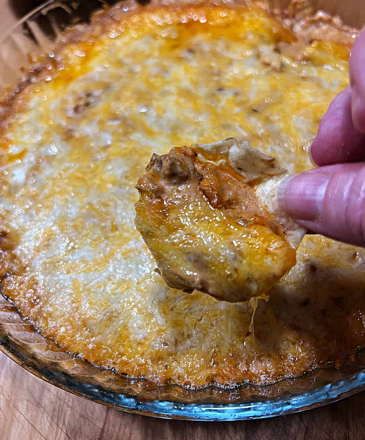 hand holding a tortilla chip with a scoop of hot taco dip, ready to eat.