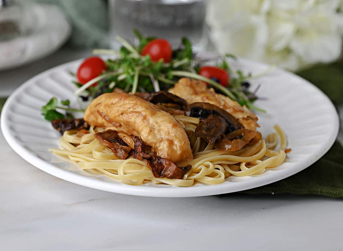 A plate of chicken marsala served on fettucini noodles with a green salad on the side.