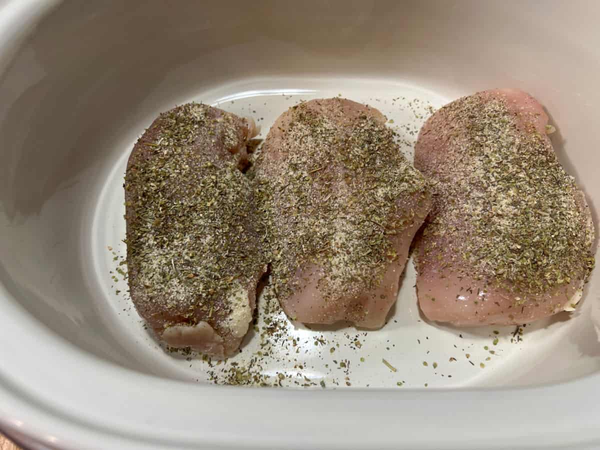 Chicken breasts in slow cooker sprinkled with seasonings.