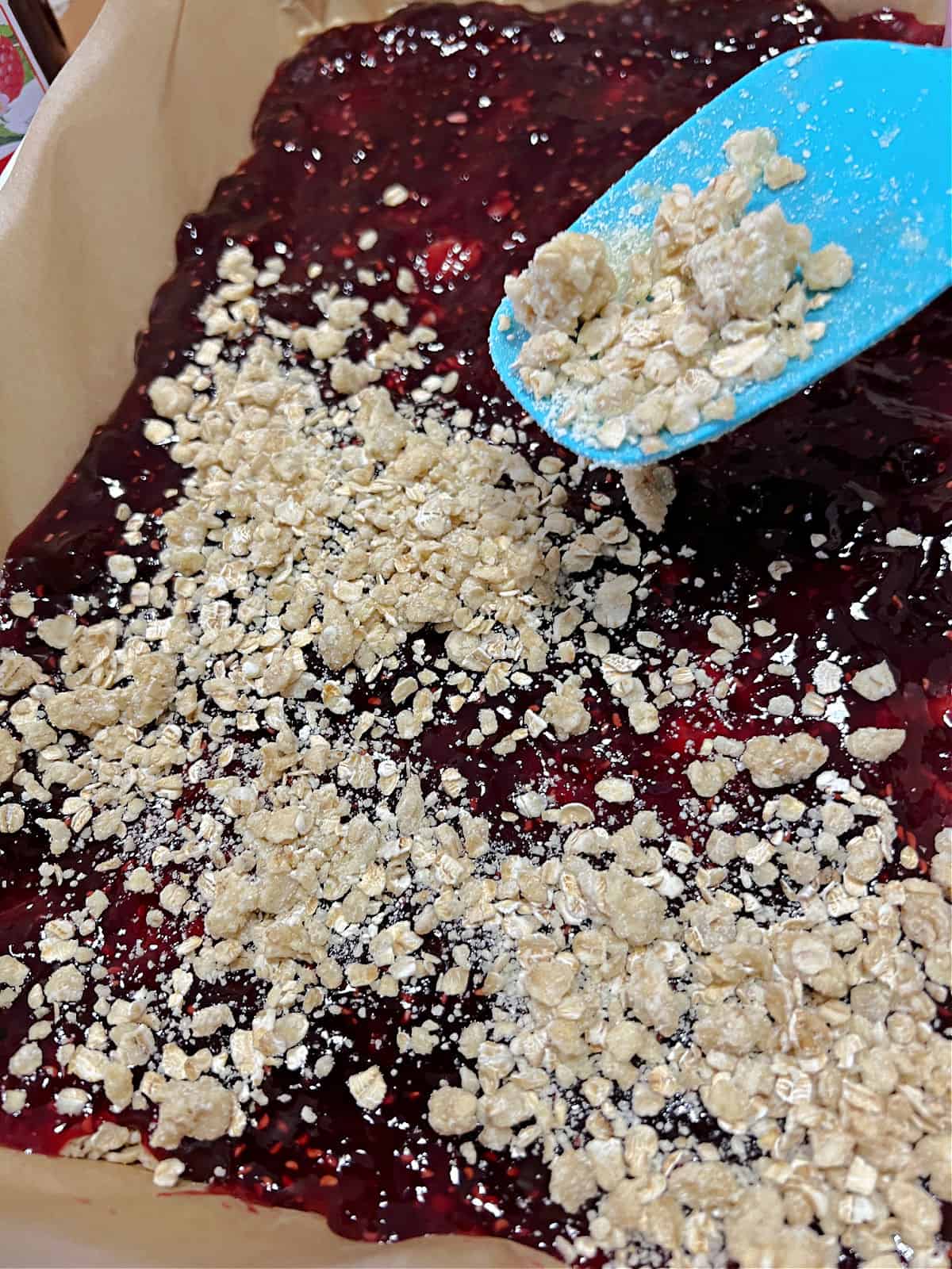 Sprinkling oat mixture on top of the jam layer.