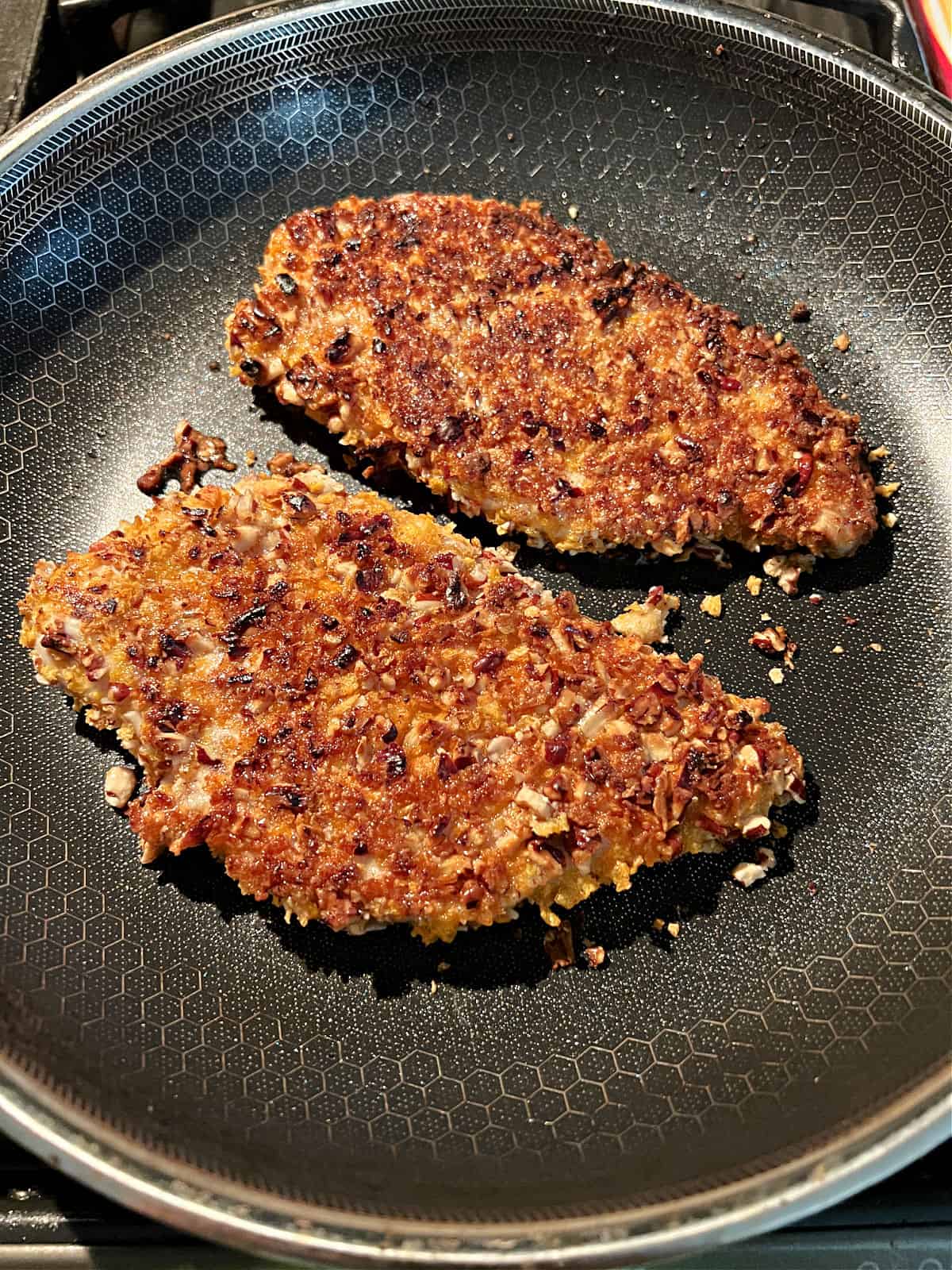 Pecan coated chicken breasts cooking in the pan.