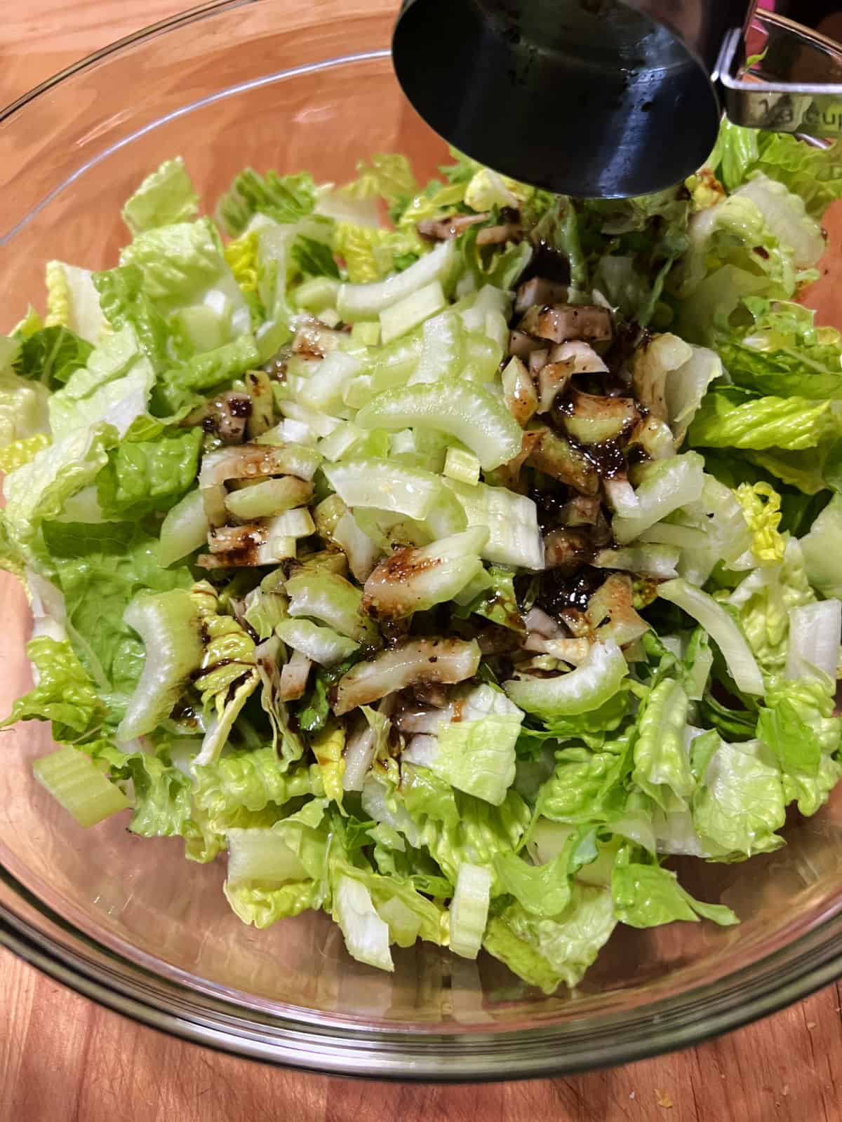Adding balsamic dressing to a bowl of lettuce and celery.