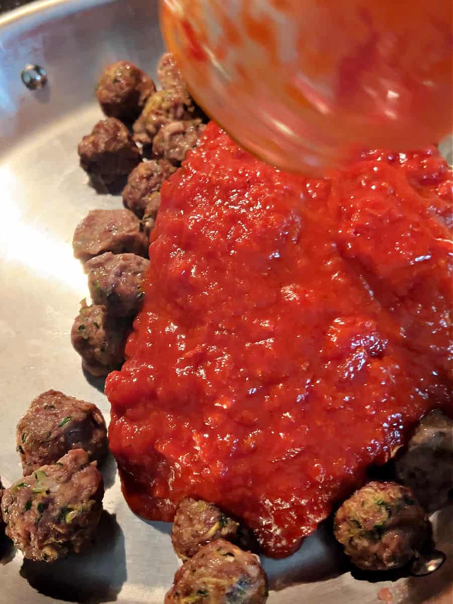 Adding meatballs and sauce to a large skillet.