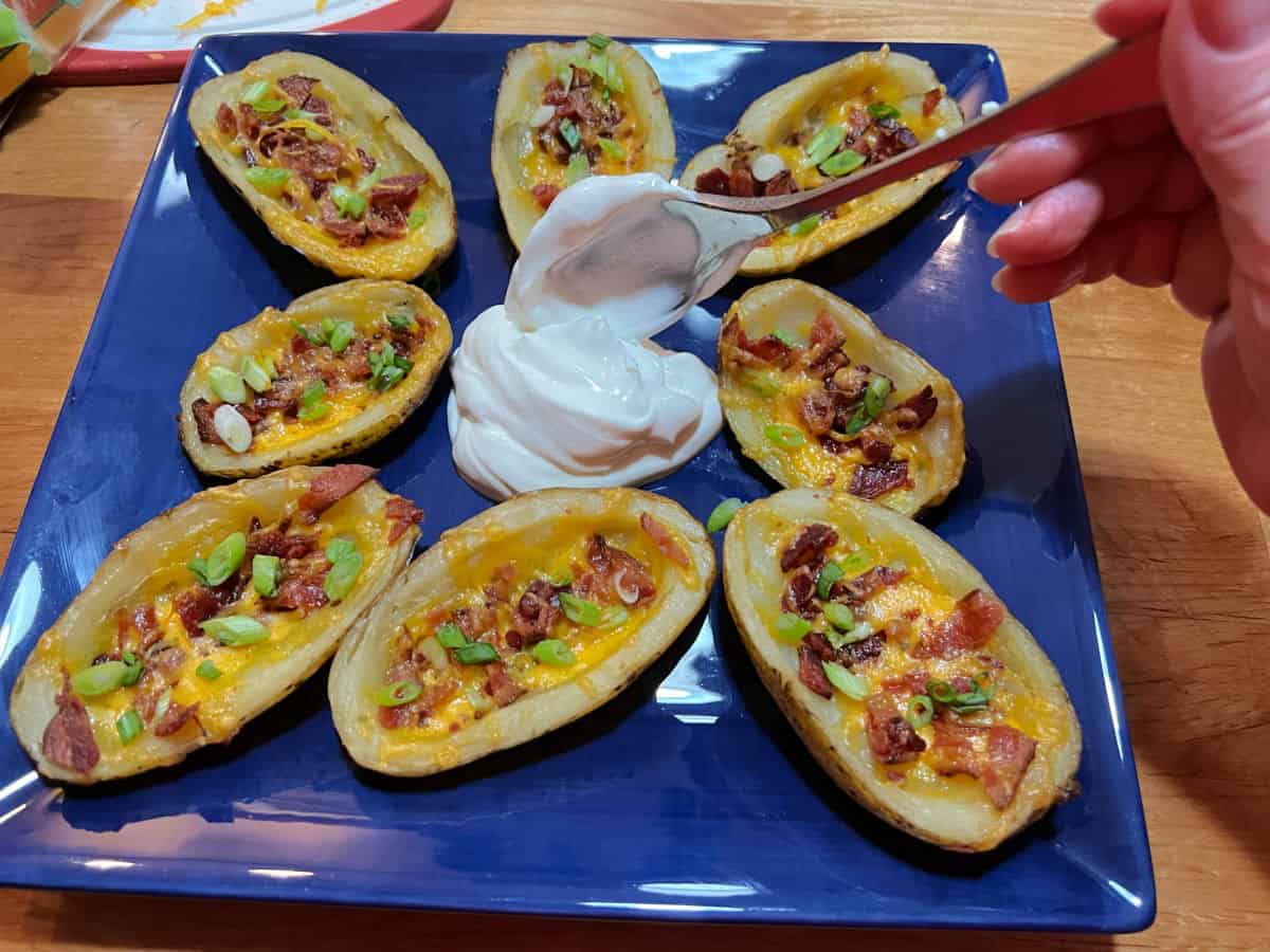 blue plate of loaded potato skins, a scoop of sour cream being added for dipping.