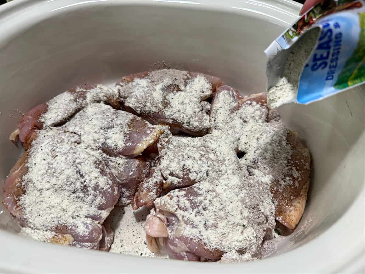 raw chicken in crockpot with dry seasoning sprinkledon top.