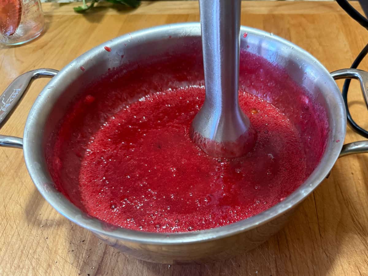 using an immersion blender to blend up the pieces in the sauce.