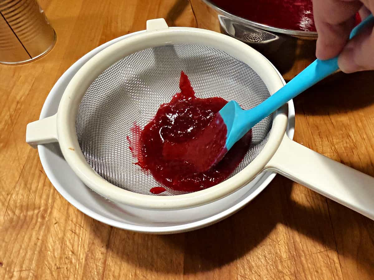 using a strainer and spatula to strain the skins from the sauce.