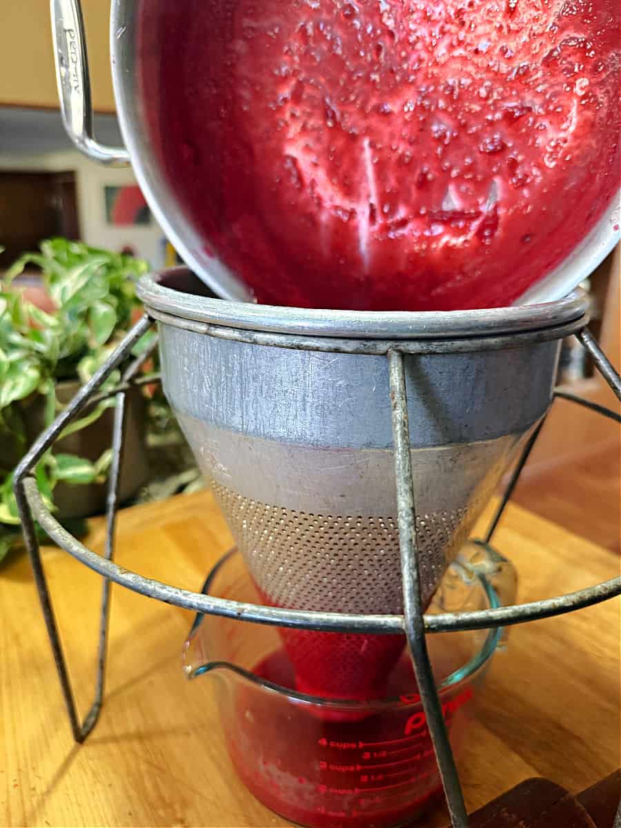 Old fashioned cone shaped strainer being used to strain the cranberry sauce.