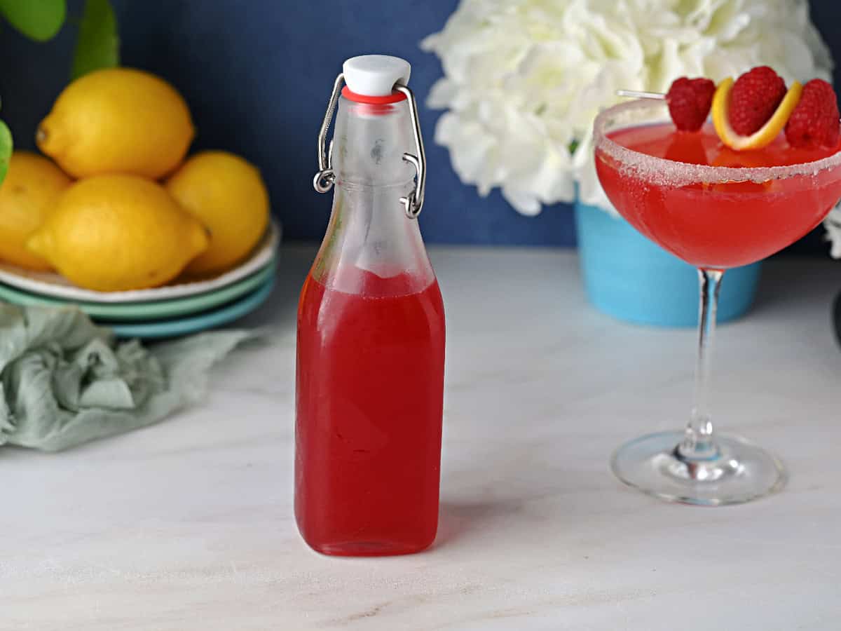 A bottle of homemde raspberry simple syrup next to a martini made with it.