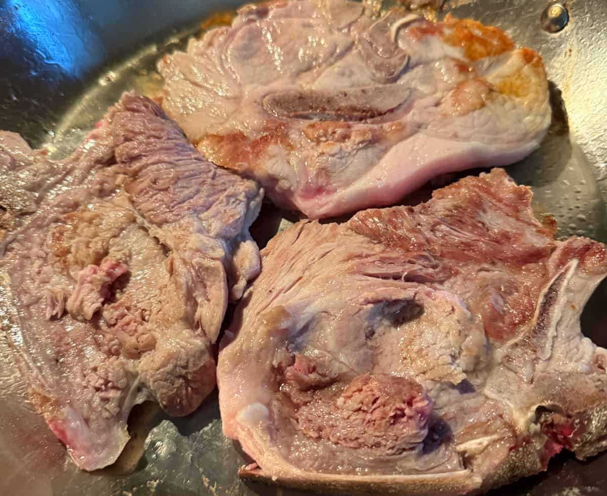 Lightly browned pork chops in a skillet.