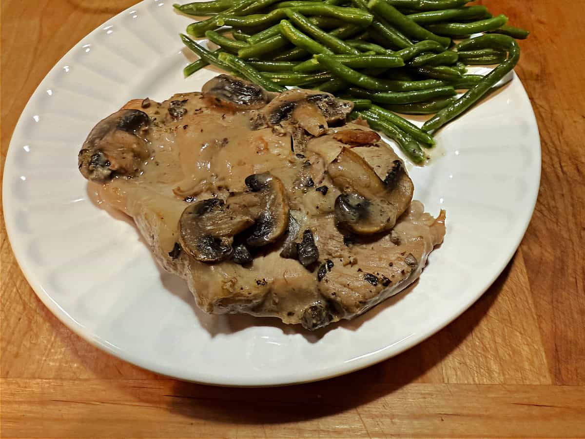 Pork chop on a plate with the mushroom sauce covering and green beans on the side.