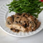 A pork chop smothered with mushroom gravy on a plate with green beans.
