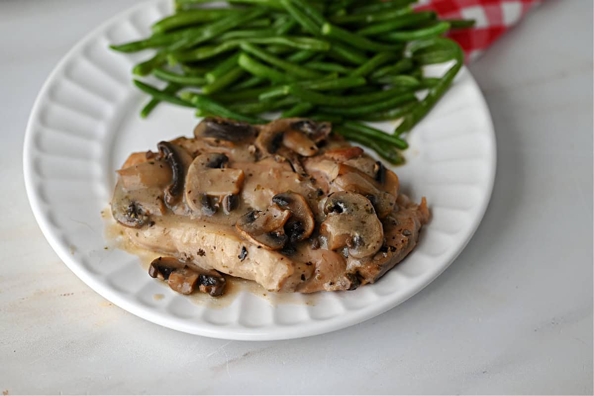 A plate with a pork chop covered in mushroom gravy, with green beans on the side.