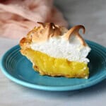 A slice of lemon meringue pie, on a small blue plate, ready to eat.