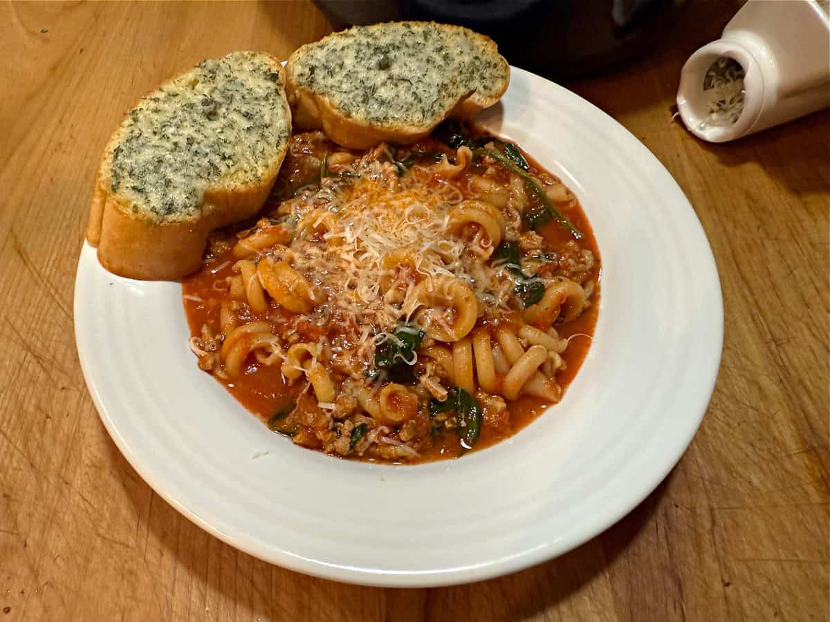 A bowl of lasgna soup topped with Parmesan cheese and served with garlic bread.