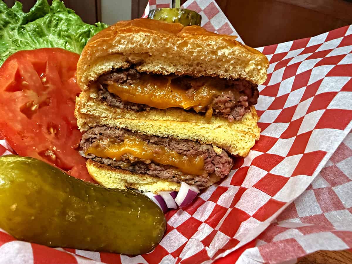 Stuffed burger in a basket with pickle and toppings.