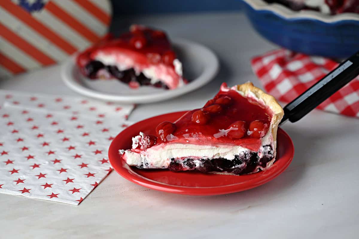a slice of no bake berry cream pie known as Miss American Pie, showing the red white and blue layers.
