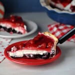 a slice of red white and blue layered pie, also known as Miss American Pie, showing the layers of blueberry and cherry with cream cheese filling in between.