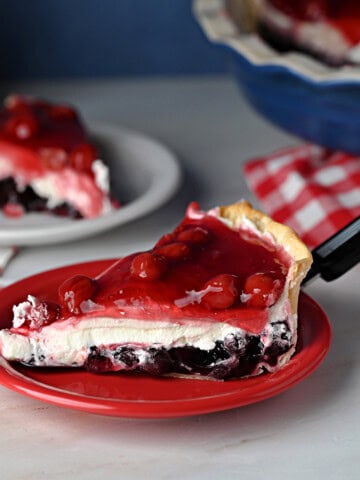 a slice of red white and blue layered pie, also known as Miss American Pie, showing the layers of blueberry and cherry with cream cheese filling in between.
