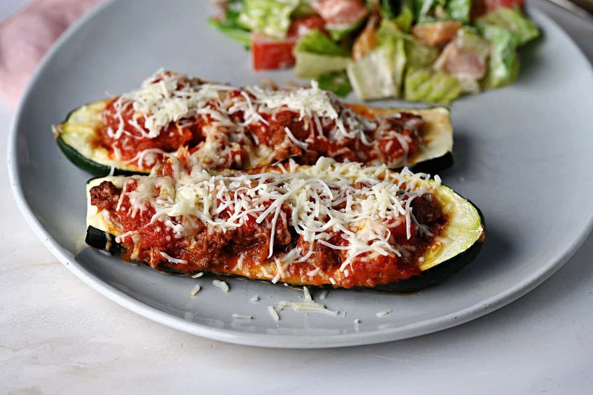 two zucchini boats stuffed with ground beef in sauce and served with salad.