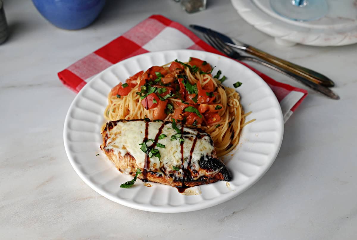 a plate of bruschetta chicken with angel hair pasta.