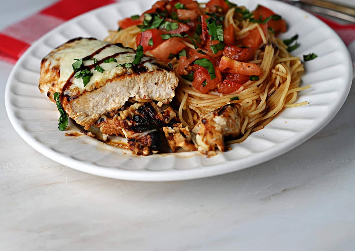 a plate of Bruschetta chicken and pasta, the meat is cut and ready to take a bite!