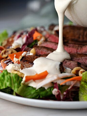 drizzling homemade blue cheese dressing onto a steak salad.