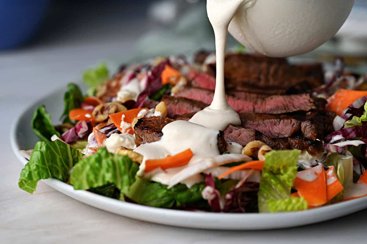 drizzling homemade gorgonzola blue cheese dressing onto a salad.
