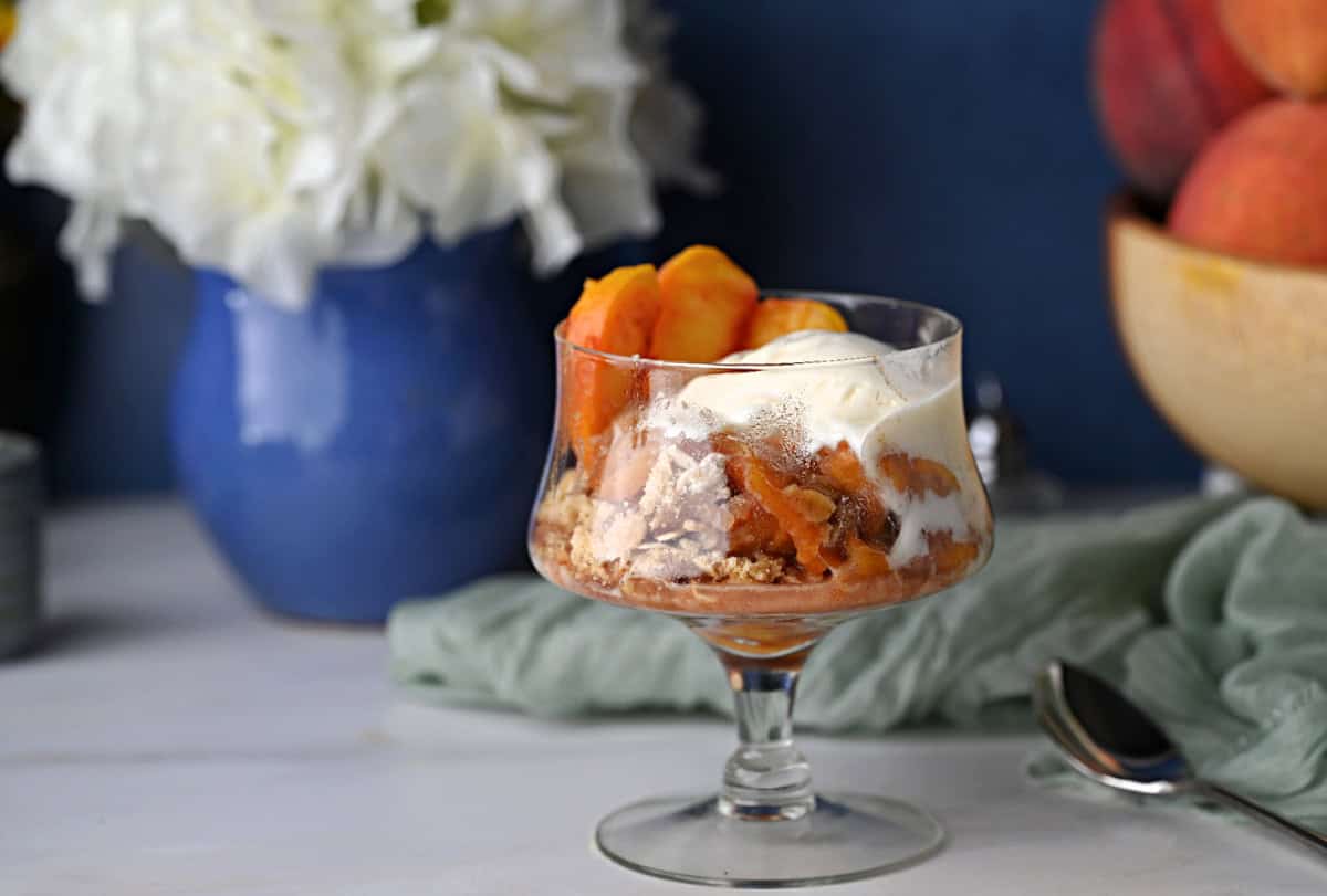 a serving of peach crisp with a scoop of ice cream in a stemmed glass.