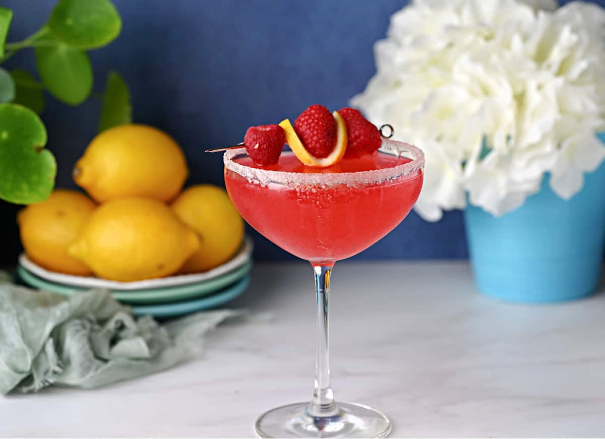 raspberry lemon drop martini garnished with fresh raspberries and a lemon slice.