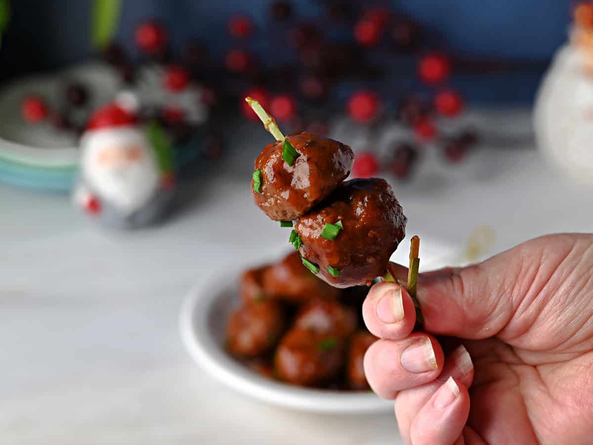 2 cranberry meatballs on a skewer held up by a hand, ready to eat.