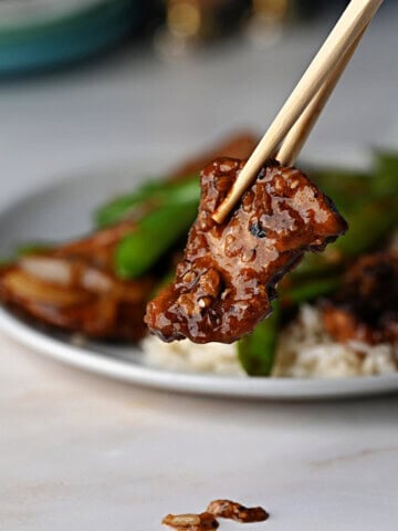 a piece of pork stir fry held by chopsticks with the full plate behind.