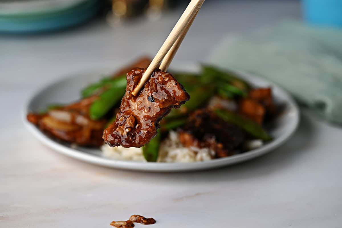 chop sticks holding a piece of pork stir fry.